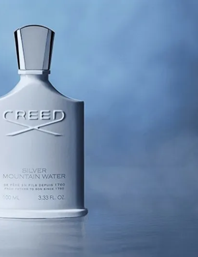 A sleek silver Creed fragrance bottle on a reflective surface with a blue background.