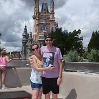 Couple posing happily in front of a castle at a theme park.