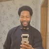 Man with afro hairstyle taking a selfie in a bathroom mirror.