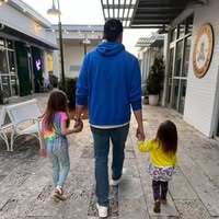 A man walking hand-in-hand with two young girls in a shopping area.